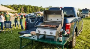 Compact portable propane grill set up on a tailgate table for outdoor camping and game day tailgating.