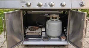 The spacious lower storage cabinet of a top rated 4 burner grill under 500 dollars containing a propane tank.