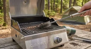 Grill brush cleaning the stainless steel grates of a portable tabletop gas grill after cooking
