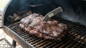 Inserting a digital meat probe into a cooked brisket inside an offset charcoal smoker for backyard brisket.