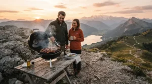 A portable pellet grill for camping and tailgating positioned on a rocky overlook with a panoramic mountain view at sunset.
